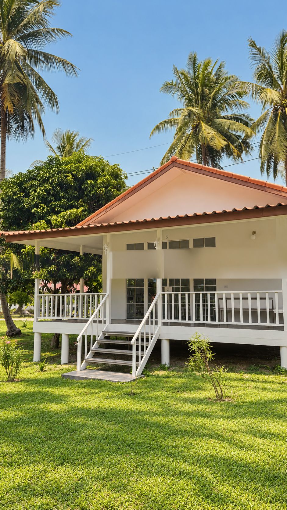 Elevated white bungalow with veranda and steps, framed by coconut palms