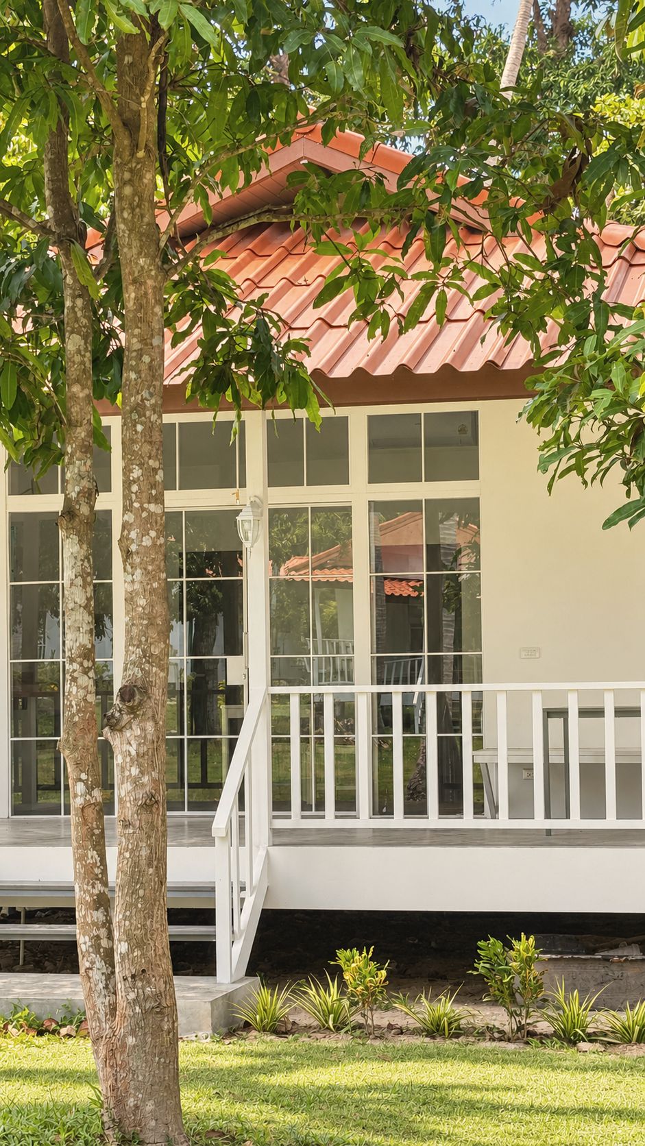 Bungalow veranda glimpsed through the trunks of garden trees